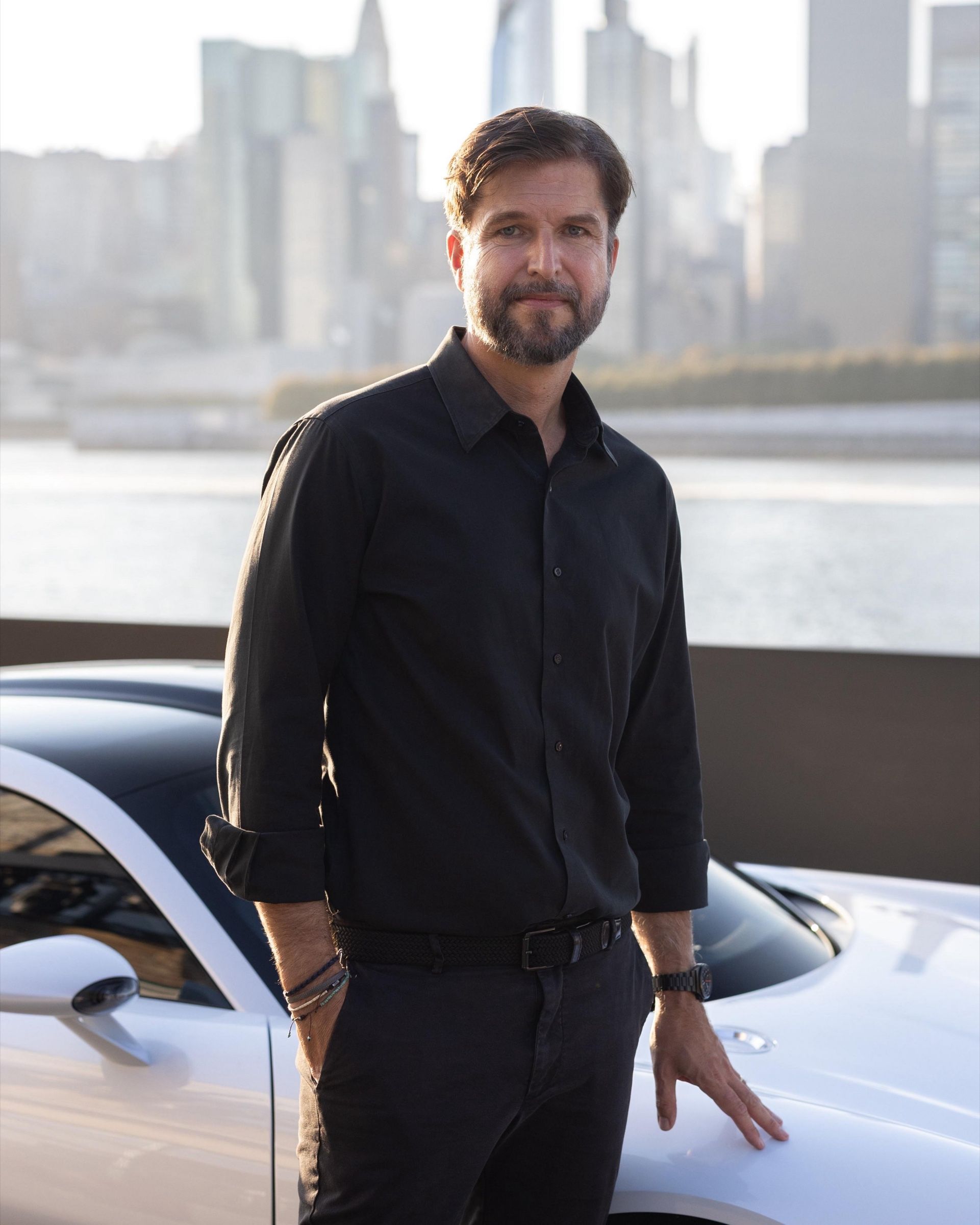 Portrait of Tobias Sühlmann with the car and the skyline behind him